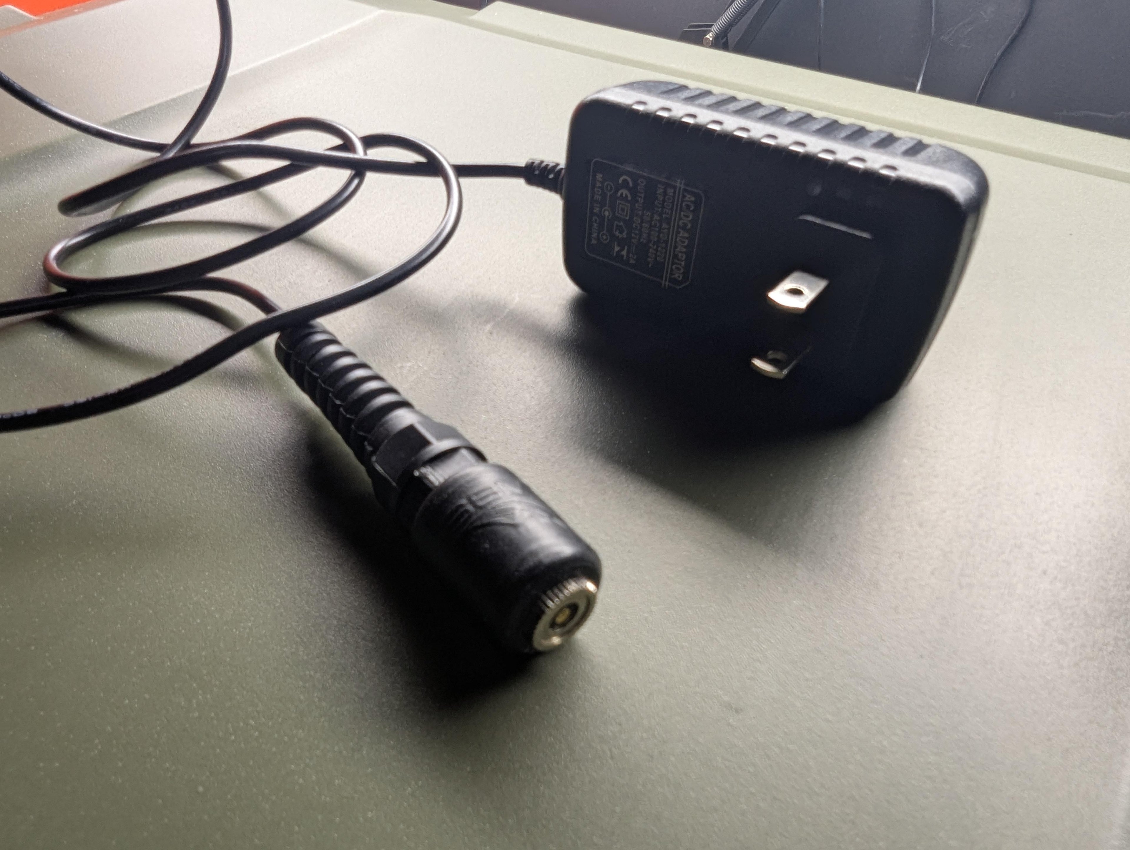 RC-1 charger cable coiled beside the included 12V 2A AC/DC wall adapter