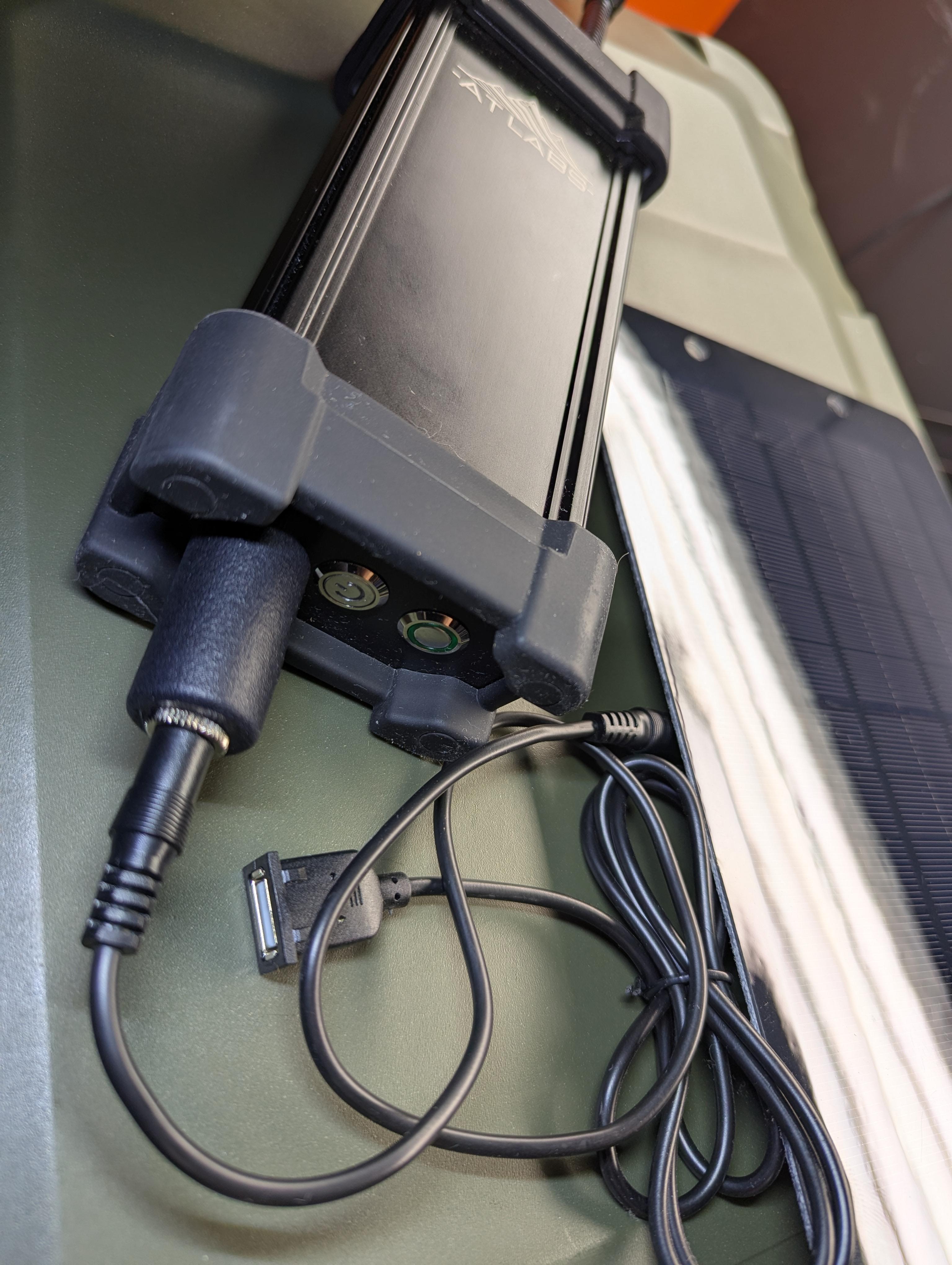AT Labs RC-2 rapid charger running an RM-1/RM-2 radio off a portable solar panel via its 12V DC barrel input. Off-grid charging with no wall outlet. Solar panel and radio sold separately, not included with the charger.